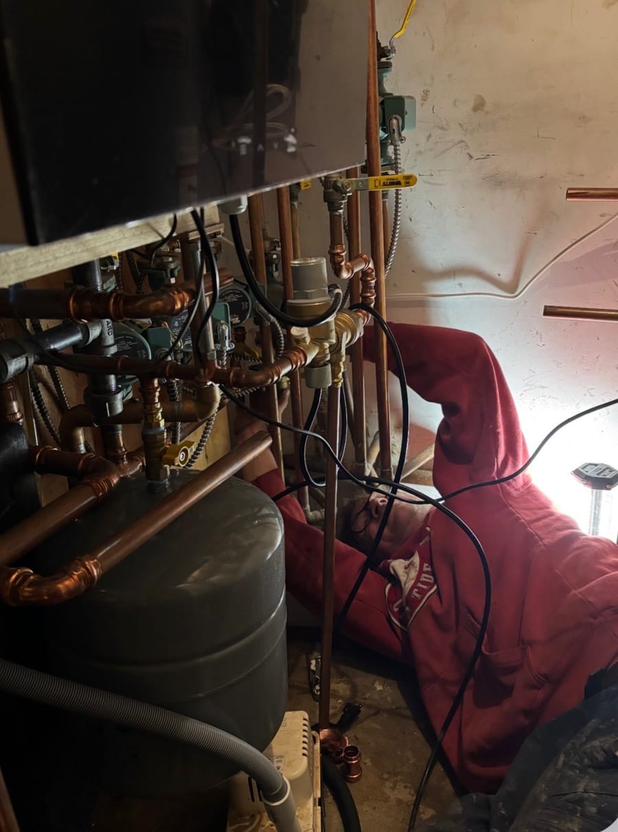 Matt Hough working beneath a copper manifold in a basement mechanical room
